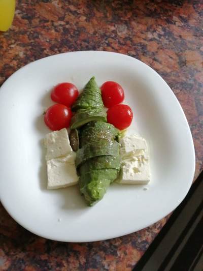 Small avocado sliced in two with a sprinkle of olive oil 2 cubes Greek feta cheese and 2 small Cherry tomatoes